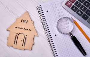 Drveni model kućice, sveska sa beleškama, lupa i kalkulator na stolu