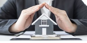 Osoba drži sklopljene ruke iznad modela kuće simulirajući zaštitu